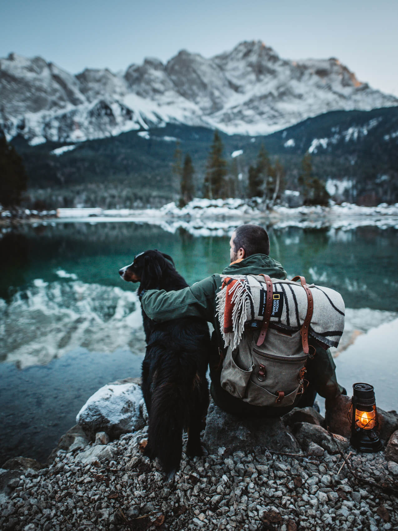 A man and his loyal dog taking in the breathtaking scenery of a mountain and lake.