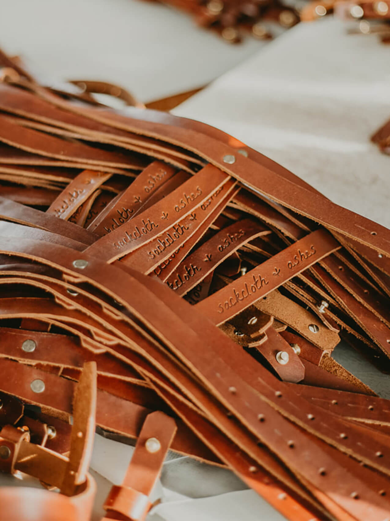 A collection of leather belts arranged in a pile on a table, showcasing different colors and textures.