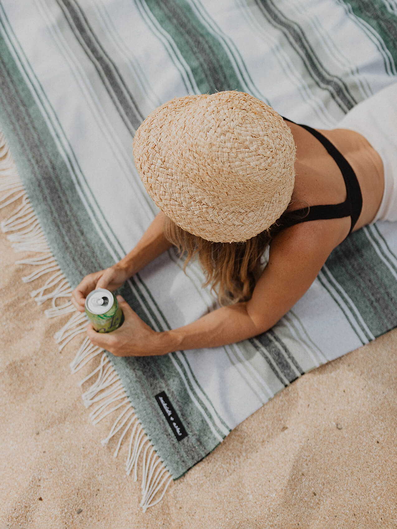 A woman in a hat and bikini enjoying the sun on a beach towel.
