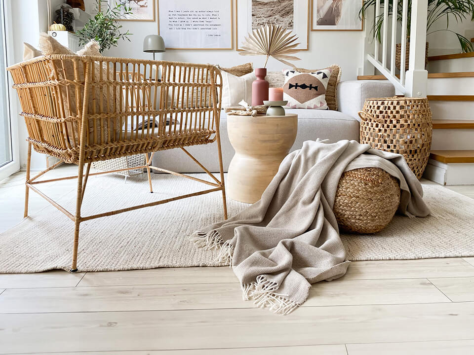 A cozy living room with a wicker chair, a stylish rug, a beautiful blanket, and a sleek white table.