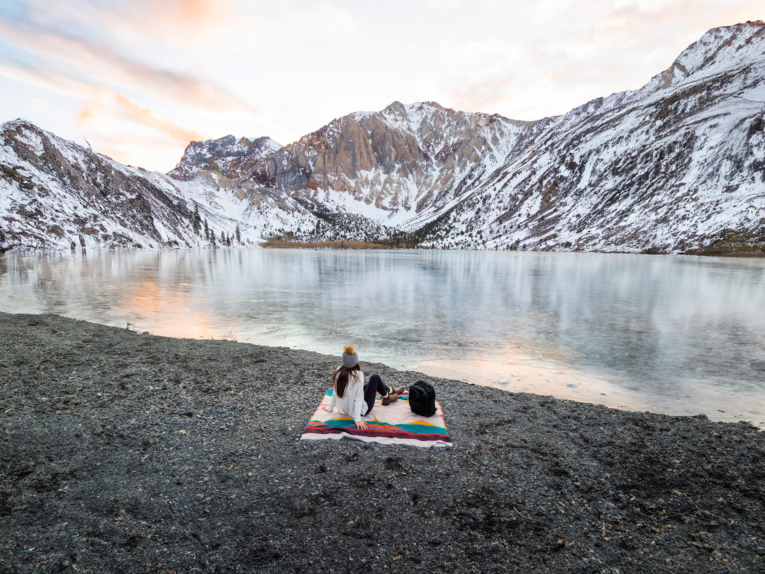 A woman enjoying a serene lakeside moment, seated on a cozy blanket.