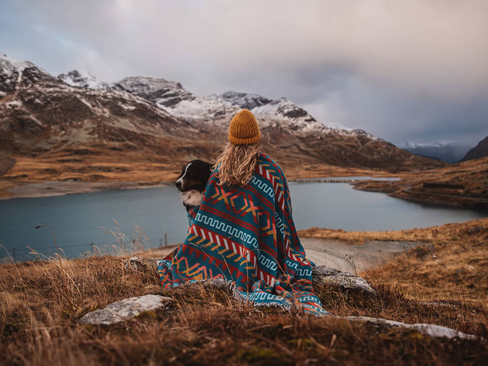 A serene woman sitting on a rock, gazing at a picturesque lake and majestic mountains in the distance.