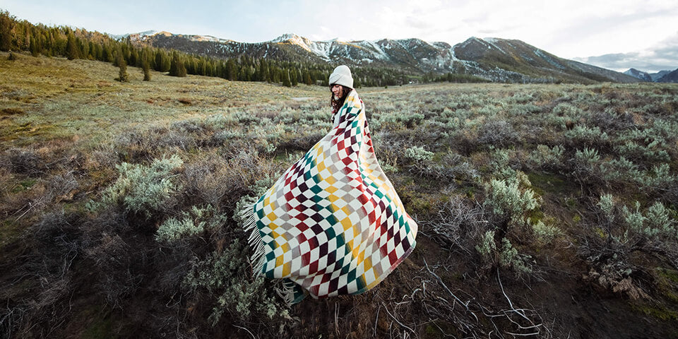 A woman standing in a field with a blanket, enjoying the beauty of nature.